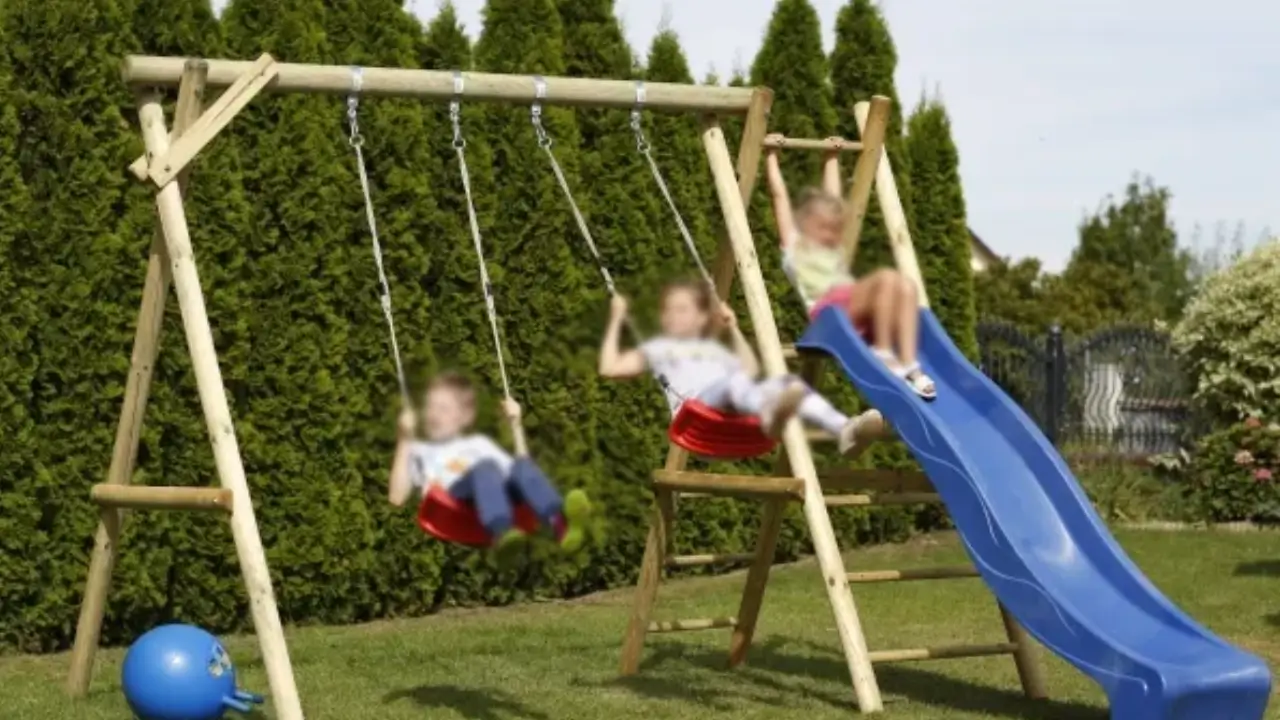 Børn leger på et gyngestativ med rutsjebane i en grøn have.